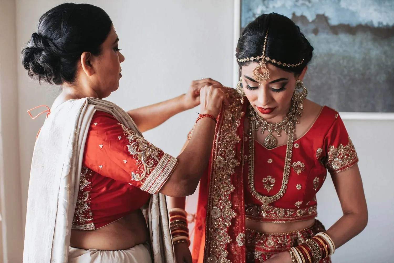Bride in red event attire being helped with jewelry